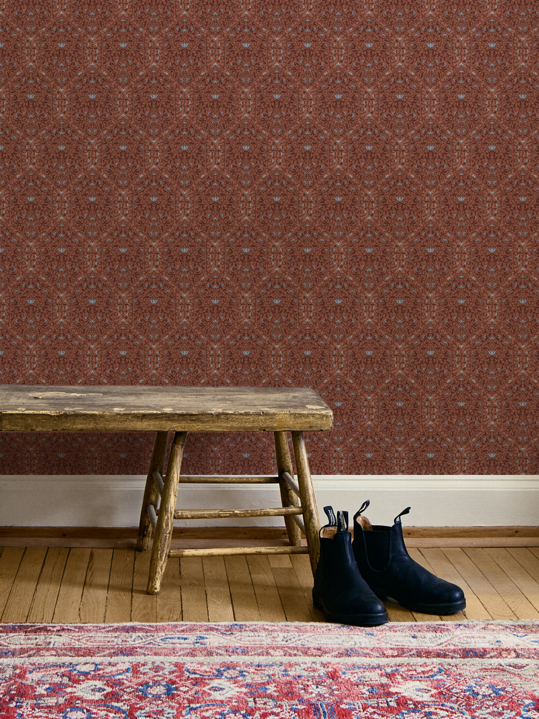 Entryway with Painted Clay Taliah Large wallpaper, wood bench, black boots and a red Persian rug