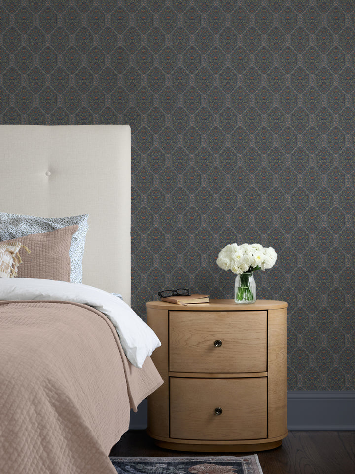 Navy Taliah wallpaper behind a cream headboard, blush quilt, oak nightstand and white peonies