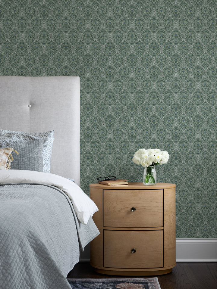 Grey-green Taliah wallpaper behind a cream headboard, grey quilt and oak nightstand